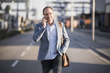 Älterer Geschäftsmann, der über sein Smartphone spricht, während er auf der Straße geht - UUF24944