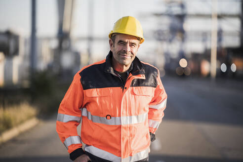 Smiling worker wearing reflective jacket at commercial dock - UUF24954