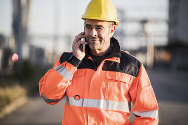 Mature male blue-collar worker talking over mobile phone at industry - UUF24955