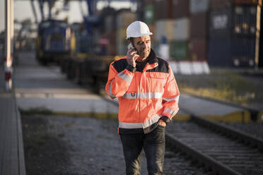 Männlicher Arbeiter mit Hand in der Tasche, der an einer Bahnstrecke mit seinem Smartphone telefoniert - UUF24962