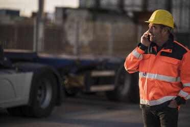 Männlicher Arbeiter mit Hand in der Tasche, der an einem kommerziellen Dock mit seinem Smartphone spricht - UUF24969