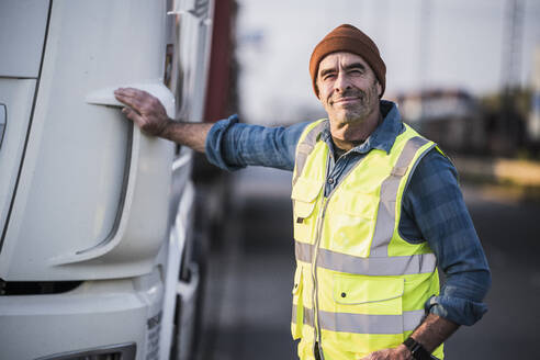 Lächelnder männlicher Fahrer neben einem Lastwagen stehend - UUF24971