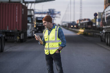 Male driver text messaging on smart phone at commercial dock - UUF24978