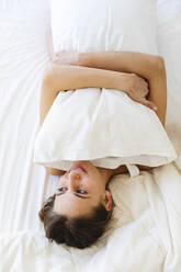 Smiling girl hugging pillow while lying on bed at home - MRAF00674