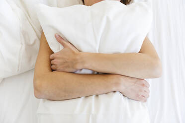 Frau umarmt weißes Kissen, während sie auf dem Bett im Schlafzimmer liegt - MRAF00675