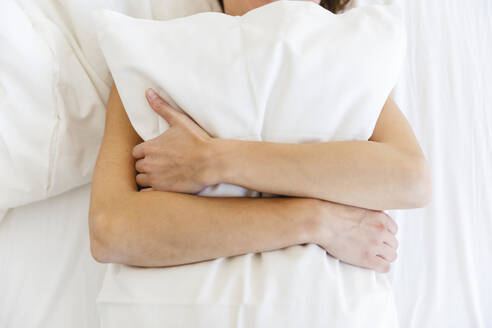 Woman embracing white pillow while lying on bed in bedroom - MRAF00675