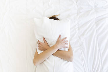Junge Frau bedeckt ihr Gesicht und umarmt ein Kissen im Schlafzimmer - MRAF00677