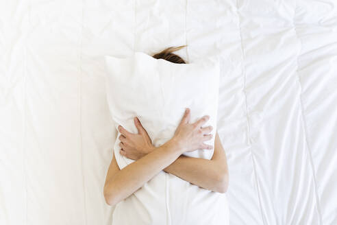 Young woman covering face while embracing pillow in bedroom - MRAF00677