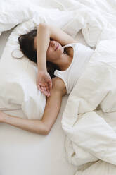 Young woman sleeping under blanket on bed in bedroom - MRAF00681