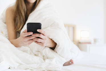 Young woman using mobile phone while sitting on bed in bedroom - MRAF00687