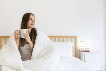 Young woman with brown hair having coffee on bed at home - MRAF00691