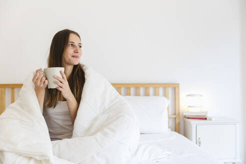 Junge Frau mit braunen Haaren beim Kaffee trinken auf dem Bett zu Hause - MRAF00691