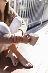 Young woman sitting with coffee cup in balcony - MRAF00696