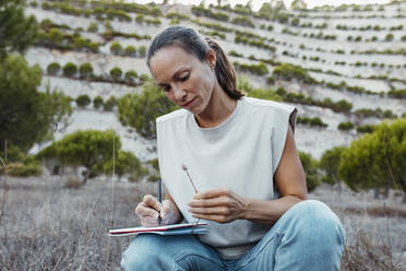 Female scientist writing in book while researching on dried grass at old mine - DMGF00587