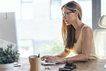 Blond female freelancer working on computer at home office - JSRF01672