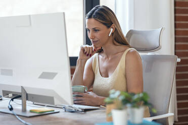 Businesswoman with hand on chin looking at computer in home office - JSRF01677