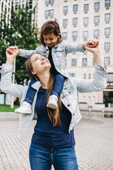 Smiling mother carrying daughter on shoulders at public park - ASGF01658