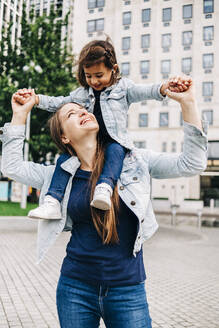 Lächelnde Mutter, die ihre Tochter in einem öffentlichen Park auf den Schultern trägt - ASGF01658
