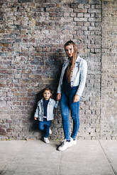 Mother and daughter standing together in front of brick wall - ASGF01660