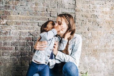 Daughter kissing mother in front of brick wall - ASGF01661