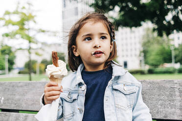 Cute girl with brown hair holding ice cream cone at park - ASGF01664