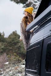 Woman with brown hair wearing knit hat while standing behind car - MRRF01634