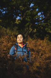 Frau mit geschlossenen Augen inmitten von Pflanzen im Wald - MRAF00712