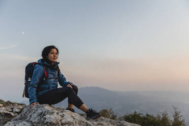 Wanderer mit Rucksack, nachdenklich auf einem Felsen - MRAF00734