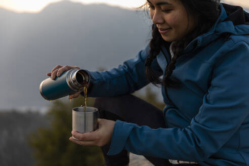Lächelnde Frau gießt Kaffee in einen Becher - MRAF00737