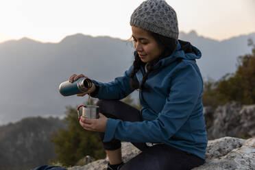 Lächelnder Wanderer, der bei Sonnenuntergang Kaffee in einen Becher gießt - MRAF00738