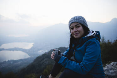 Lächelnder Wanderer mit Kaffeebecher auf einem Berg sitzend - MRAF00746