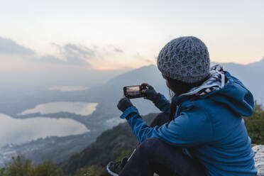 Frau fotografiert auf einem Berg mit ihrem Handy - MRAF00747