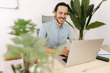 Smiling businessman using laptop at desk - TCEF02075