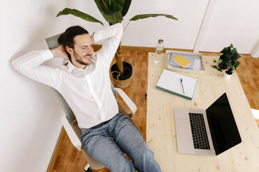 Businessman with hands behind head relaxing on chair - TCEF02083