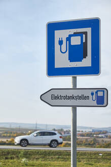 Electric vehicle charging station sign with car passing in background - BSCF00650