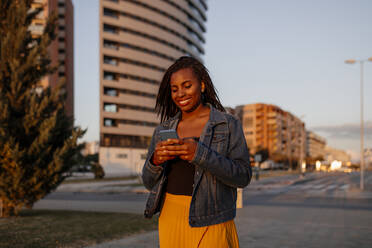 Smiling woman using mobile phone in city - DMGF00625