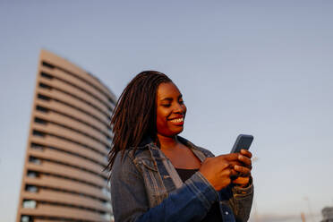 Smiling woman using smart phone in city - DMGF00626