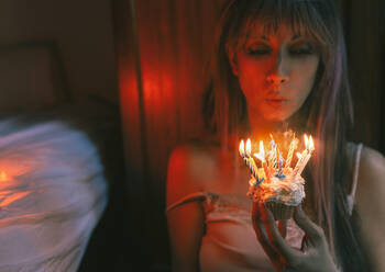 Junge Frau bläst brennende Kerzen auf einem Geburtstagskuchen zu Hause aus - EGHF00202