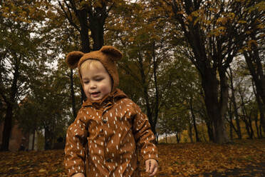 Kleinkind mit brauner Mütze und Regenmantel im Herbstpark - SSGF00145
