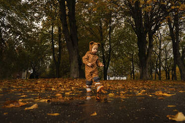 Junge in braunem Regenmantel geht im Park spazieren - SSGF00146