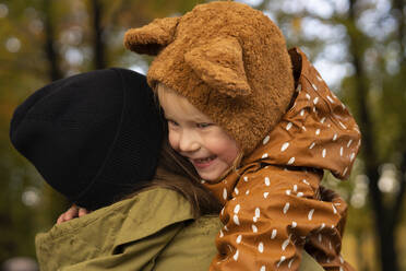 Mother with knit hat carrying daughter in park - SSGF00157