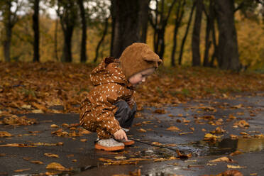 Mädchen im Regenmantel spielt in einer Pfütze auf der Straße - SSGF00165