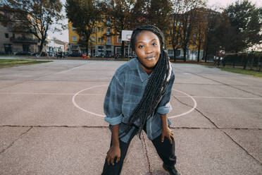 Smiling woman with locs hairstyle standing at basketball court - MEUF04591