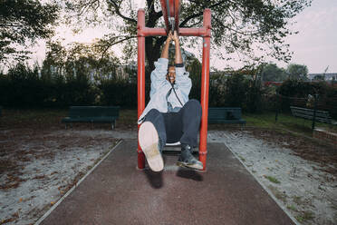 Playful woman hanging on equipment at park - MEUF04598