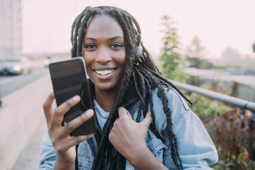 Smiling woman holding mobile phone during sunset - MEUF04615