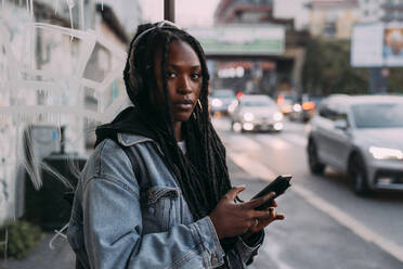 Woman with hair locs holding mobile phone on footpath - MEUF04636