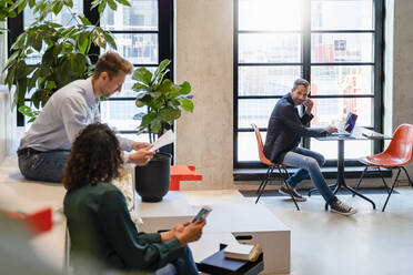 Businessman with laptop looking at colleagues in office - DIGF16589