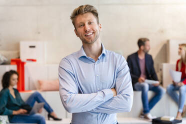 Smiling young businessman with arms crossed in office - DIGF16625