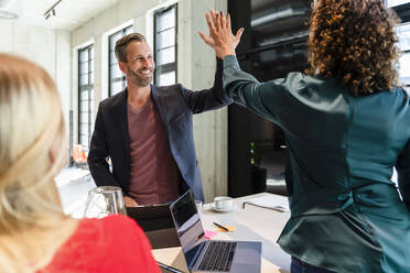 Smiling businessman giving high-five to colleague in meeting - DIGF16655