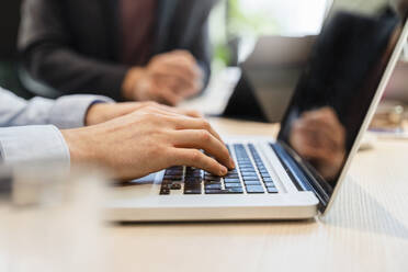 Geschäftsmann mit Laptop am Schreibtisch mit einem Kollegen im Hintergrund - DIGF16657